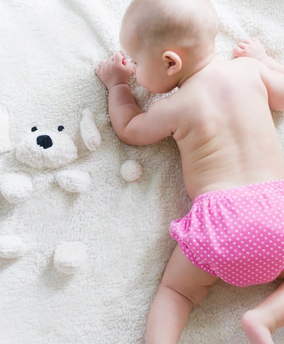 A baby lying on their tummy on a soft white blanket next to a plush bear