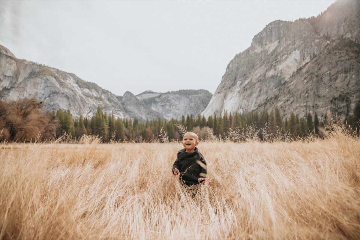 A toddler running through tall golden grass in a mountain valley