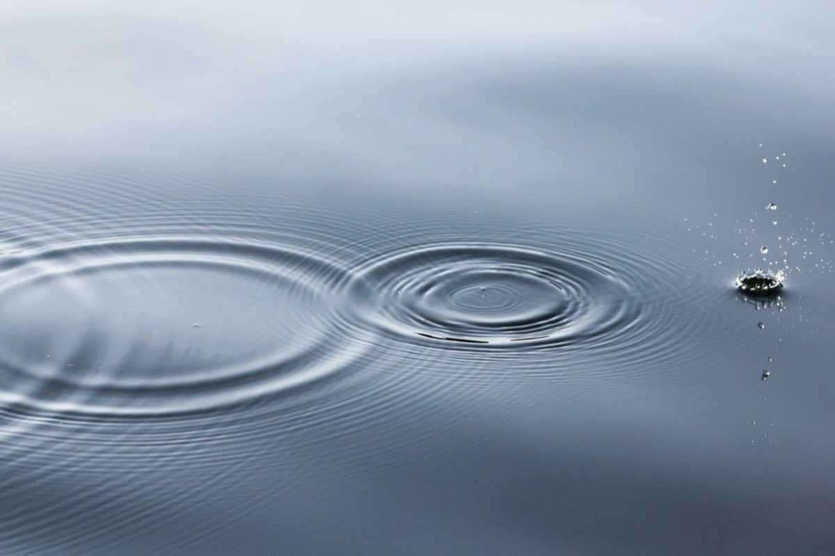 Concentric ripples spreading across still grey water